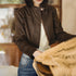Person wearing a brown denim jacket and blue jeans in an indoor setting